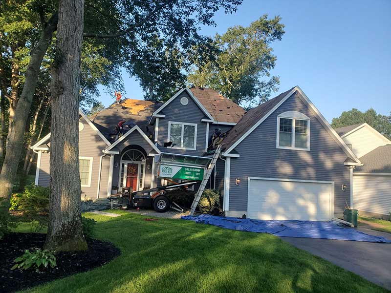 Roof Rite crew tearing off the shingles of a residential roof with their Equipter parked nearby